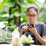 Young Asian woman  using smartphone in garden, looking on screen.