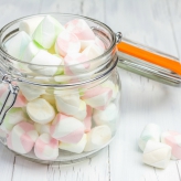 Colorful marshmallows in glass jar on light wooden background closeup